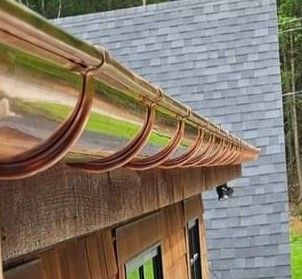 Copper gutters attached to a wooden building with gray shingle roof.