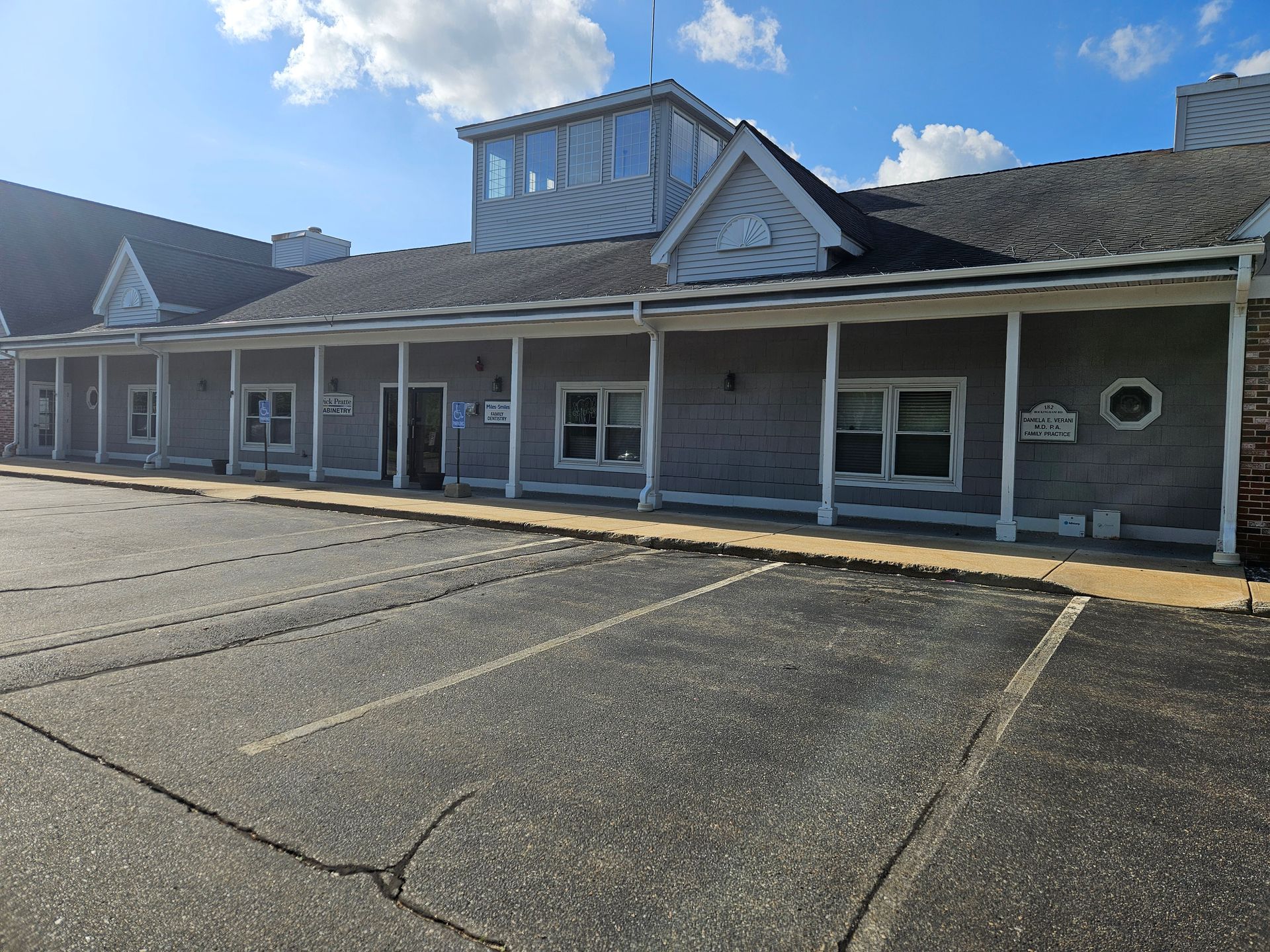 Gray building with parking in front under a blue sky. Porch and small tower present.