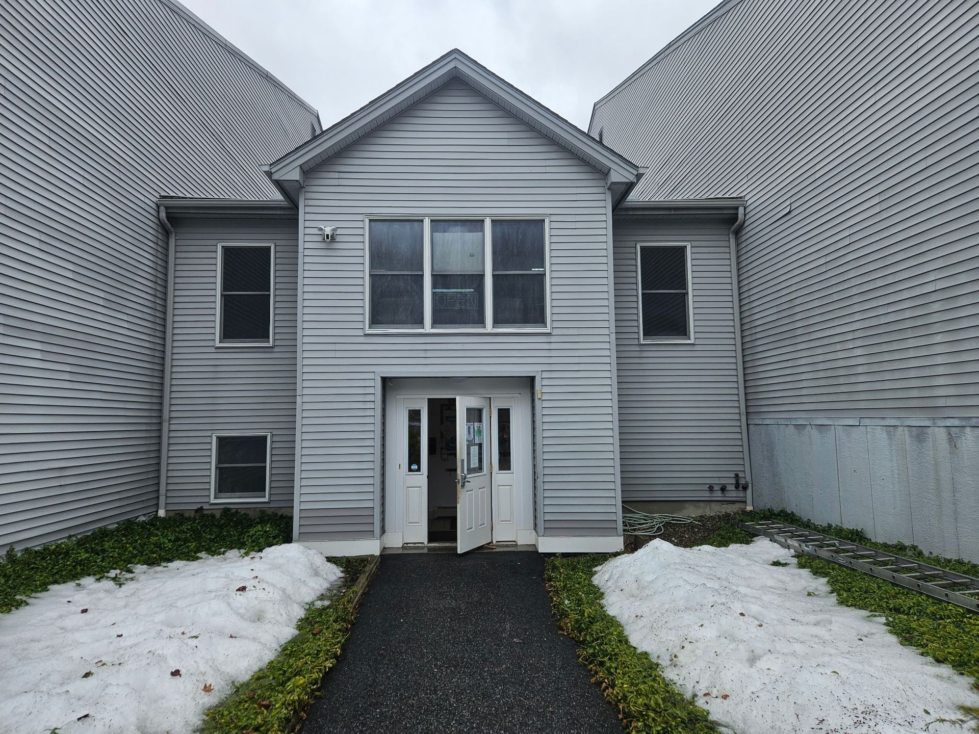 Gray building entrance between two larger structures, pathway, snow on ground.