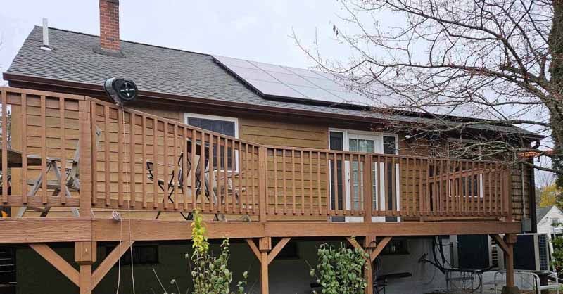 A house with a large wooden deck and solar panels on the roof.