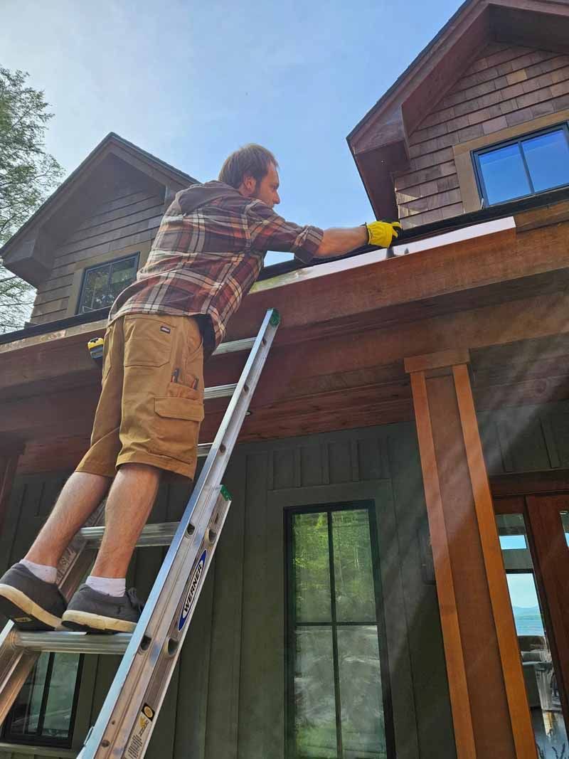 A man is standing on a ladder working on the gutters of a house.