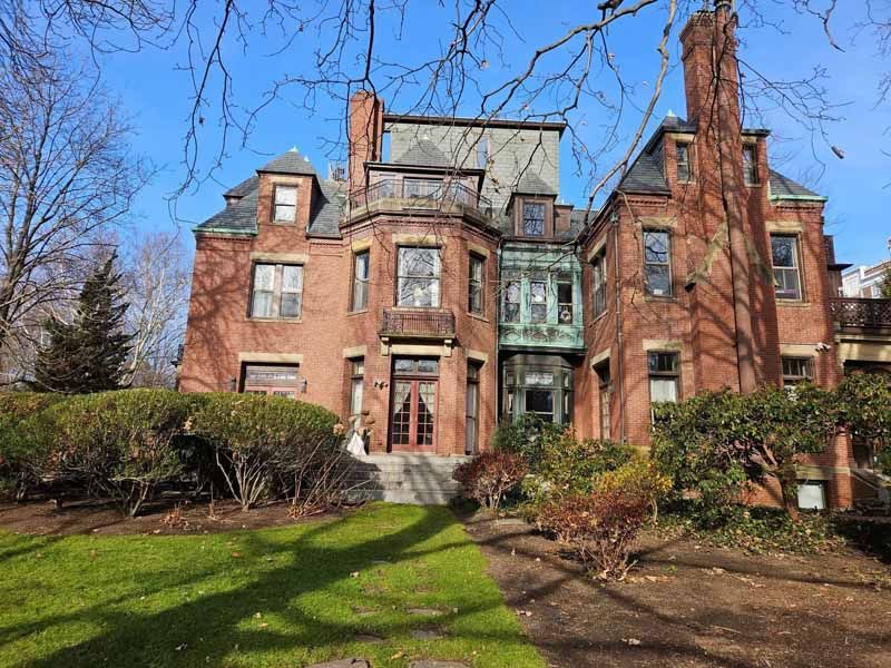 A large brick house with a lot of windows is surrounded by trees and grass.