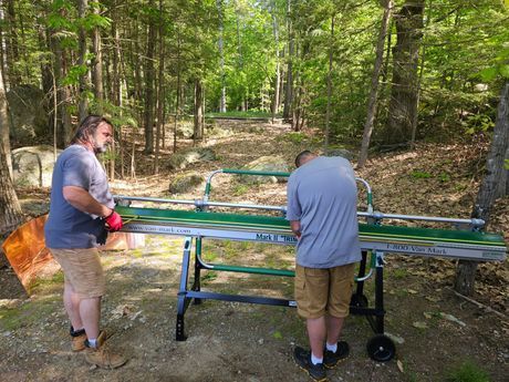 Two men are standing next to a table in the woods.