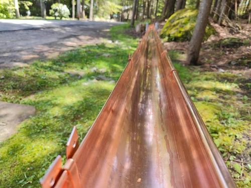 A close up of a copper gutter next to a road.