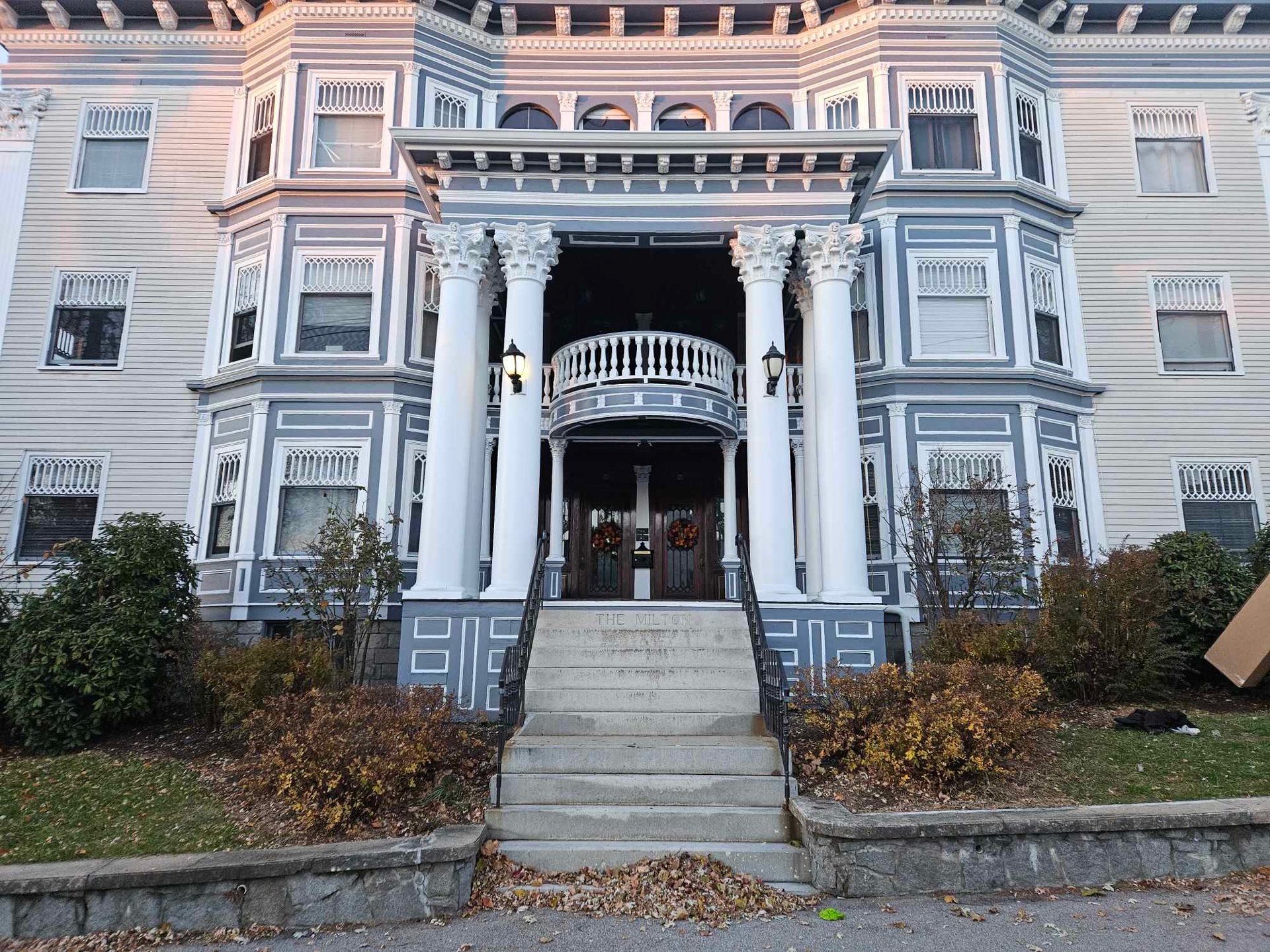 Multi-story building with a grand entrance: gray and white facade, large columns, steps leading to double doors.