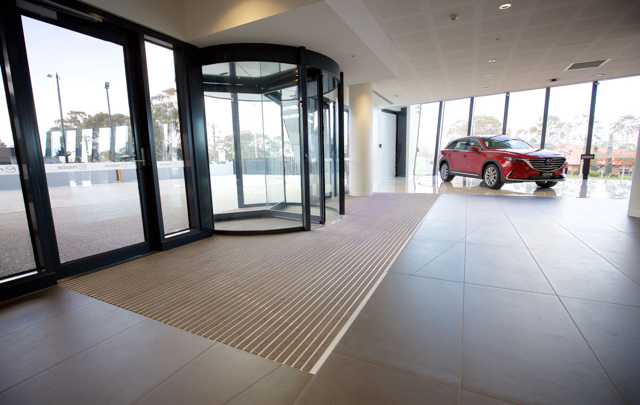 Modern building lobby with glass revolving door, tiled floor, and a red SUV outside