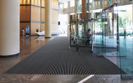 Modern office reception desk with wood slats and warm lighting, in front of glass-walled workspaces