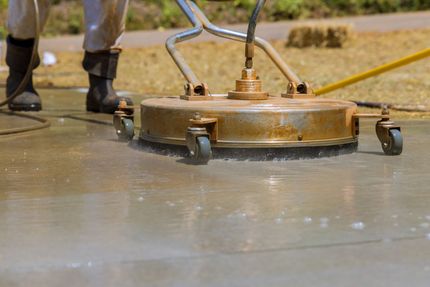 Pressure washer spraying water on a wet pavement, cleaning white paint from a speckled surface