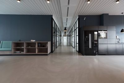 Modern office lobby with a long hallway, glass partitions, and dark cubicles on either side