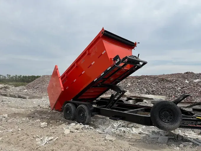 Red dump trailer tilted up, unloading debris in a rocky outdoor setting.