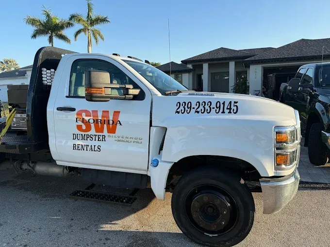White SW Florida dumpster rental truck parked outside a house with a phone number on the door.