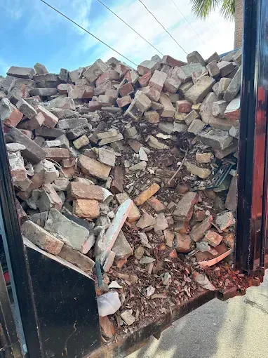 Pile of broken bricks in a black truck bed. The bricks are various sizes and colors, under a blue sky.