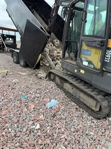 Excavator unloading rubble into a trailer on a gravel surface.
