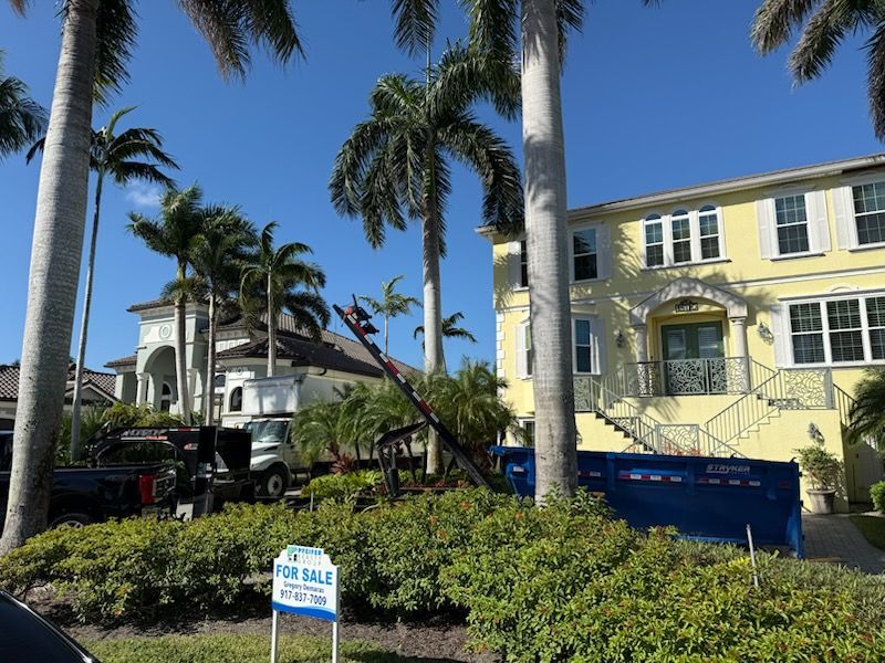 Yellow house next to palm trees. A construction dumpster and truck are in front. 