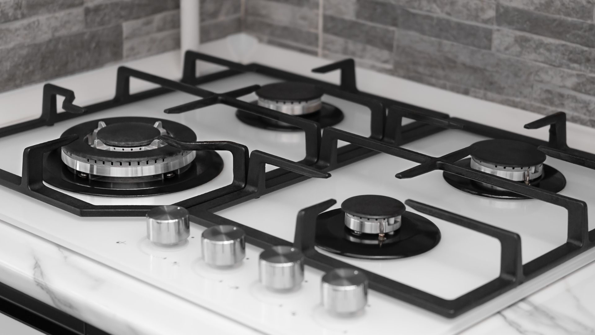 Gas stovetop with four burners, black grates, and silver knobs.