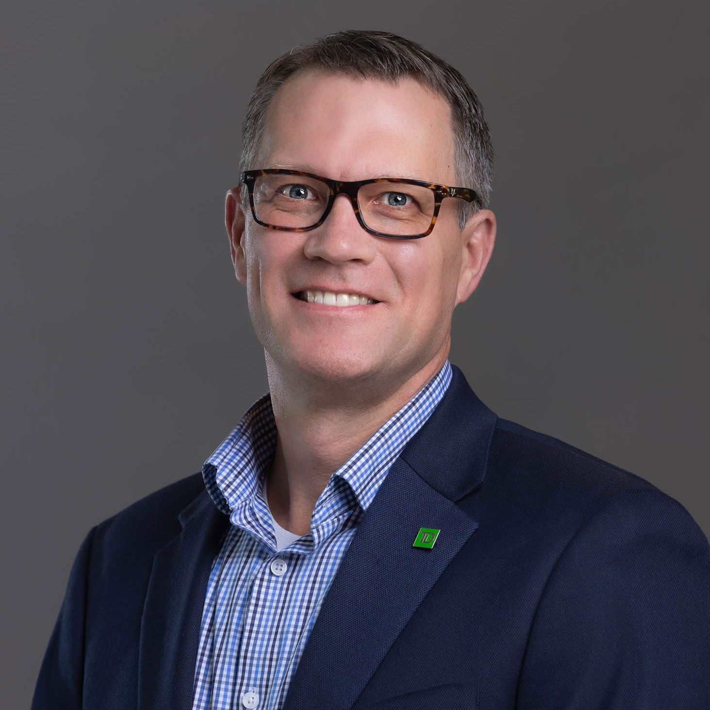 Man wearing glasses and a blue blazer smiles.