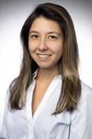 Woman with long, light-brown hair smiles, wearing a white button-down shirt.