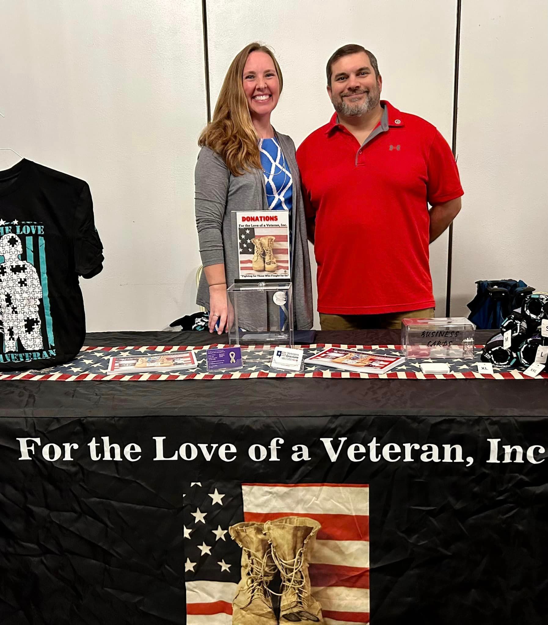 Two people stand behind a table with merchandise and a banner that reads 