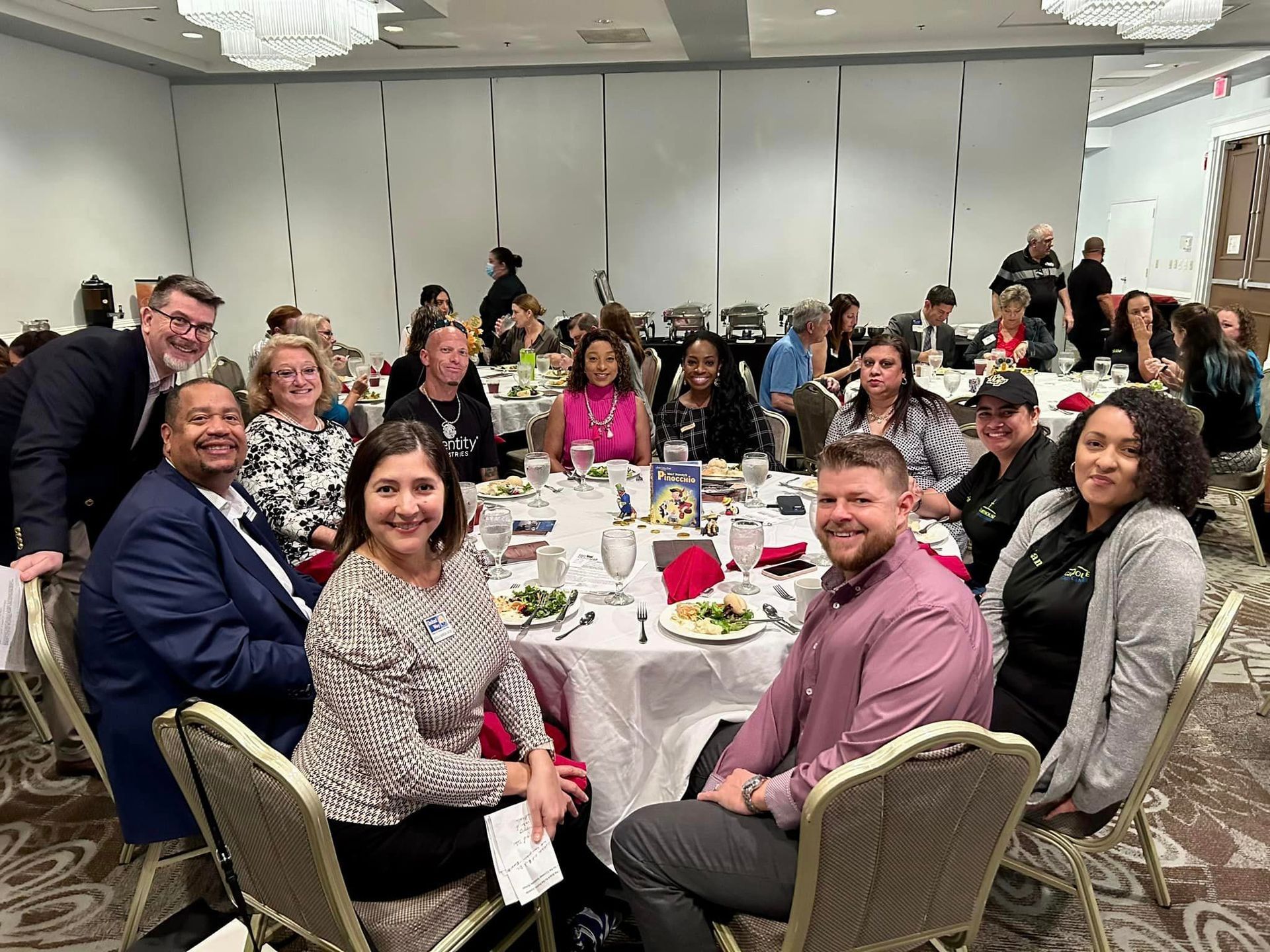 People seated at tables in a banquet hall, smiling, appearing to be at a conference or event.