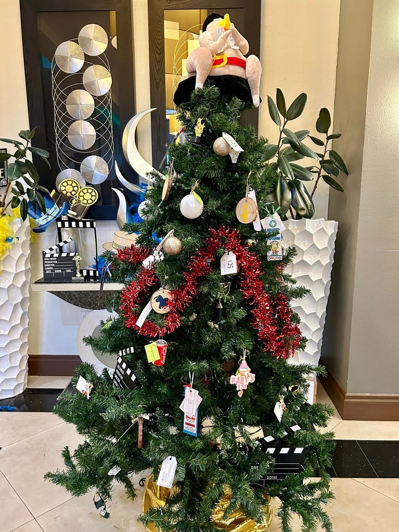 Christmas tree decorated with ornaments, tinsel, and a stuffed animal topper, in a festive setting.