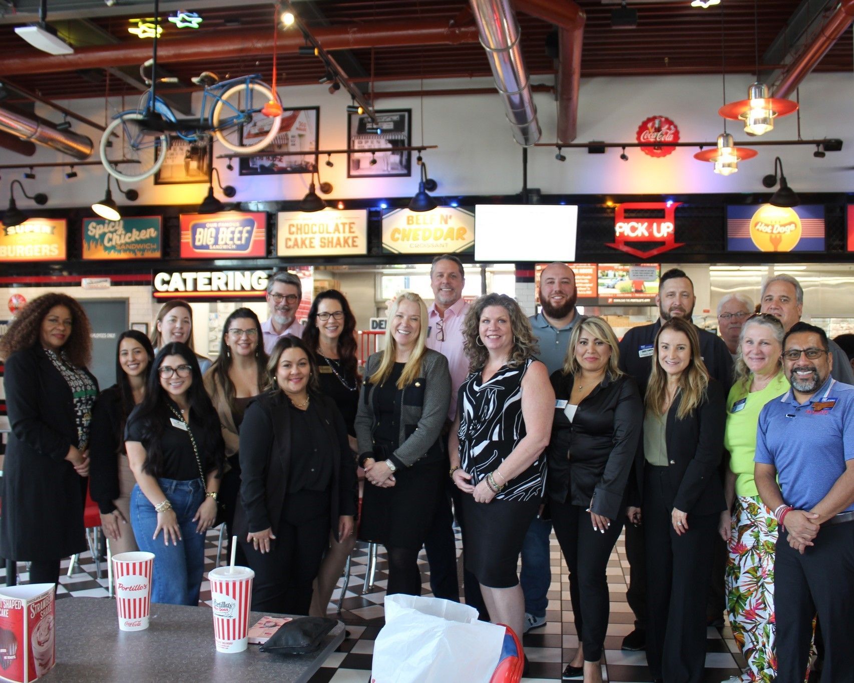 Group of people in a diner, posing for a photo. Black and white checkered floor, retro decorations.