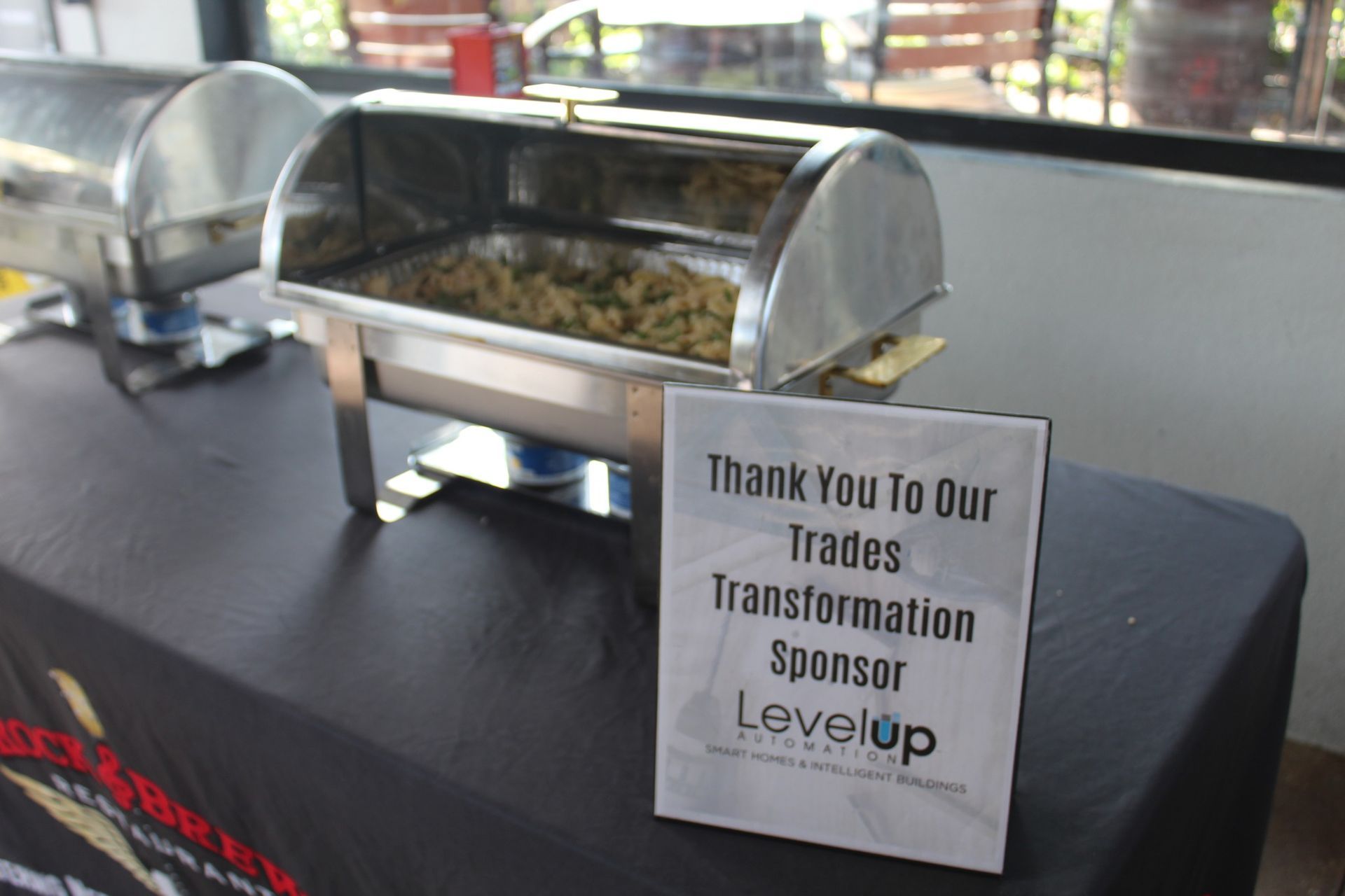 Buffet table with warming tray, food, and sponsor sign that reads