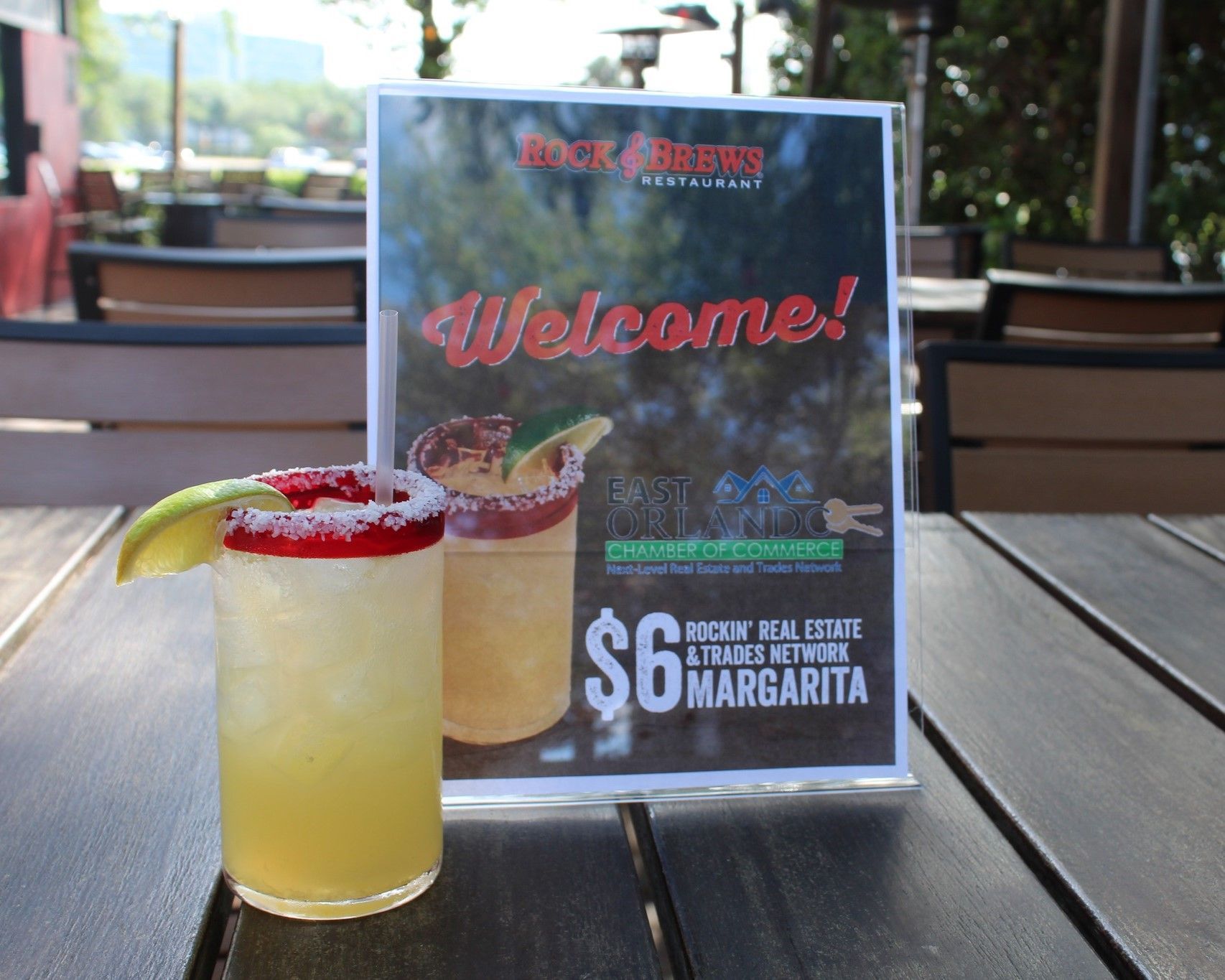 Cocktail beside a sign offering a $6 margarita. The drink has a red-salted rim and lime garnish.