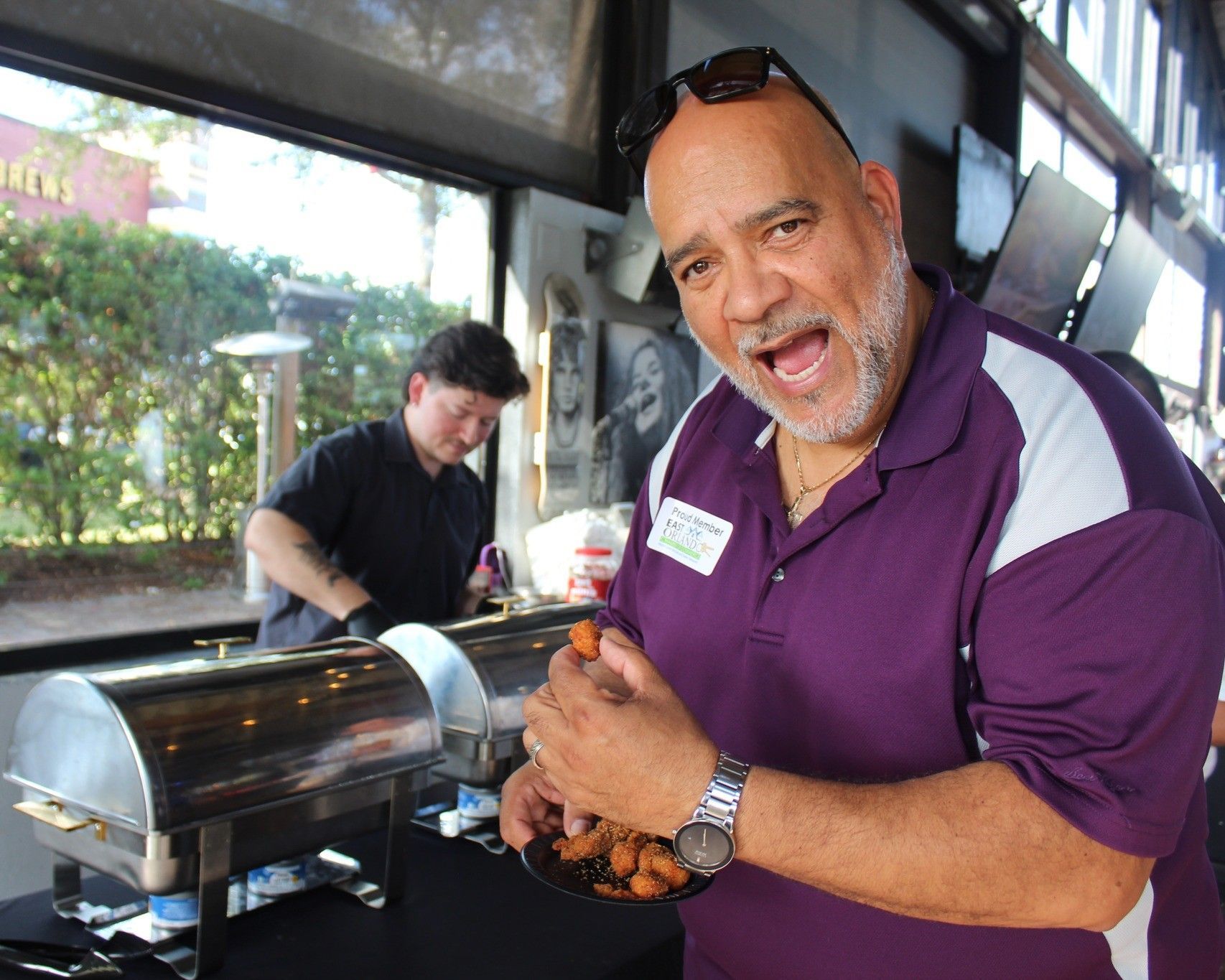 Man holding food from a buffet, smiling widely. A server works behind the buffet.