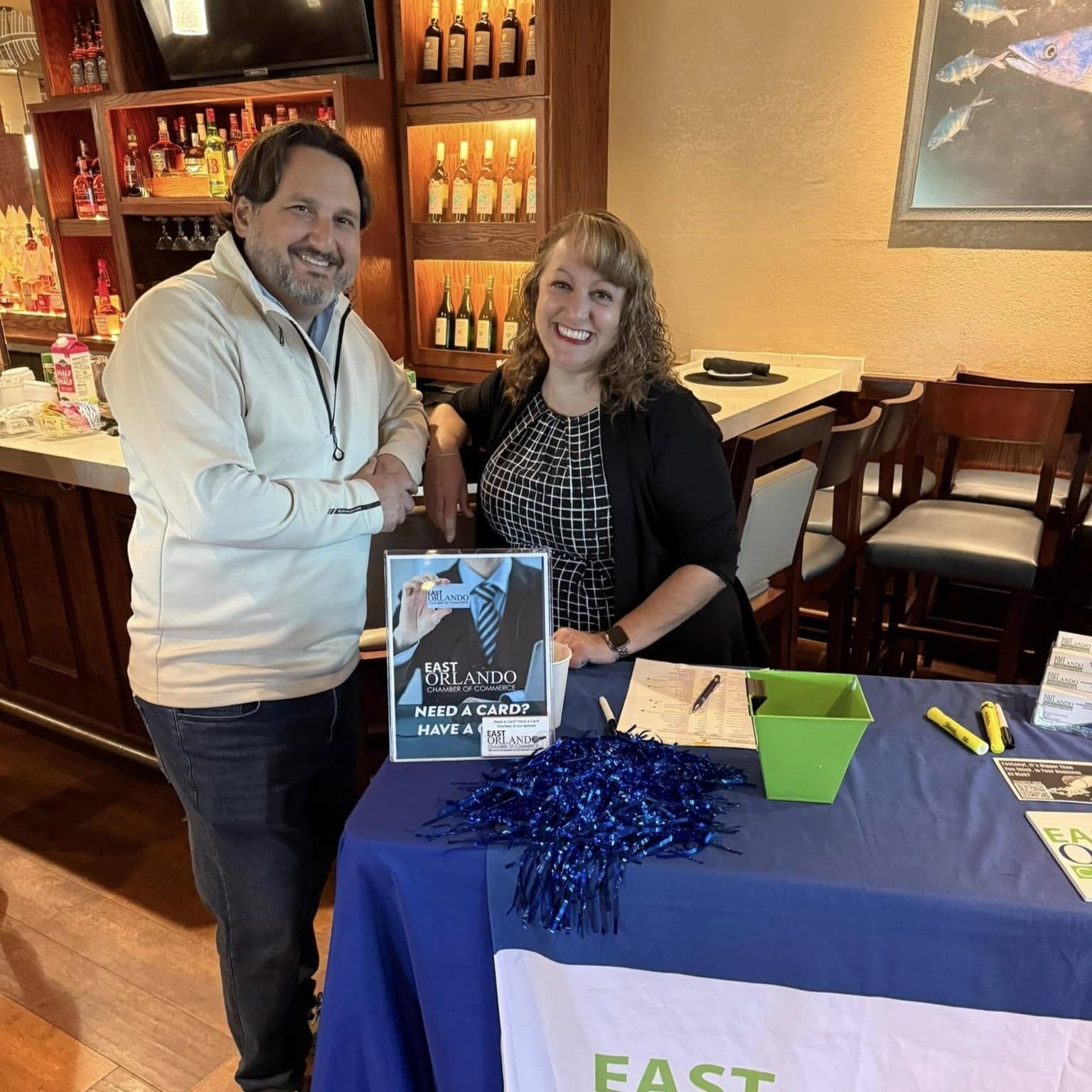 Two people at a table, smiling. Sign says 