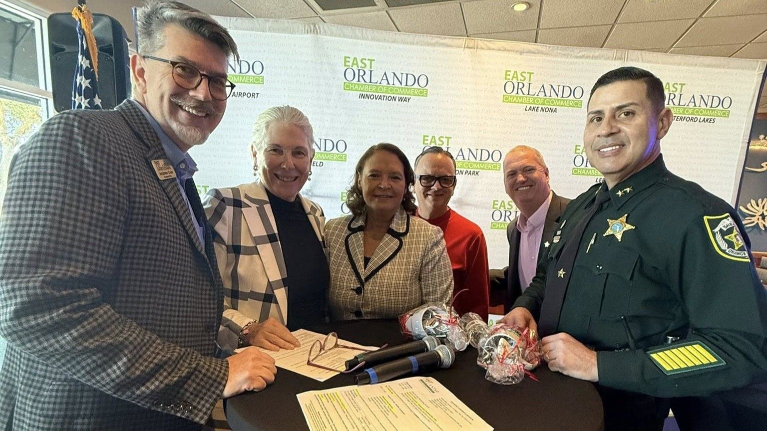 People at a signing event in East Orlando. Smiling, they stand around a table with a document and microphones.