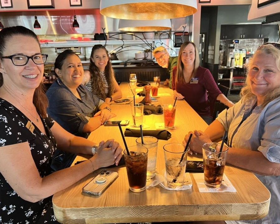 Group of six people smiling at a restaurant table. They are with drinks and food.