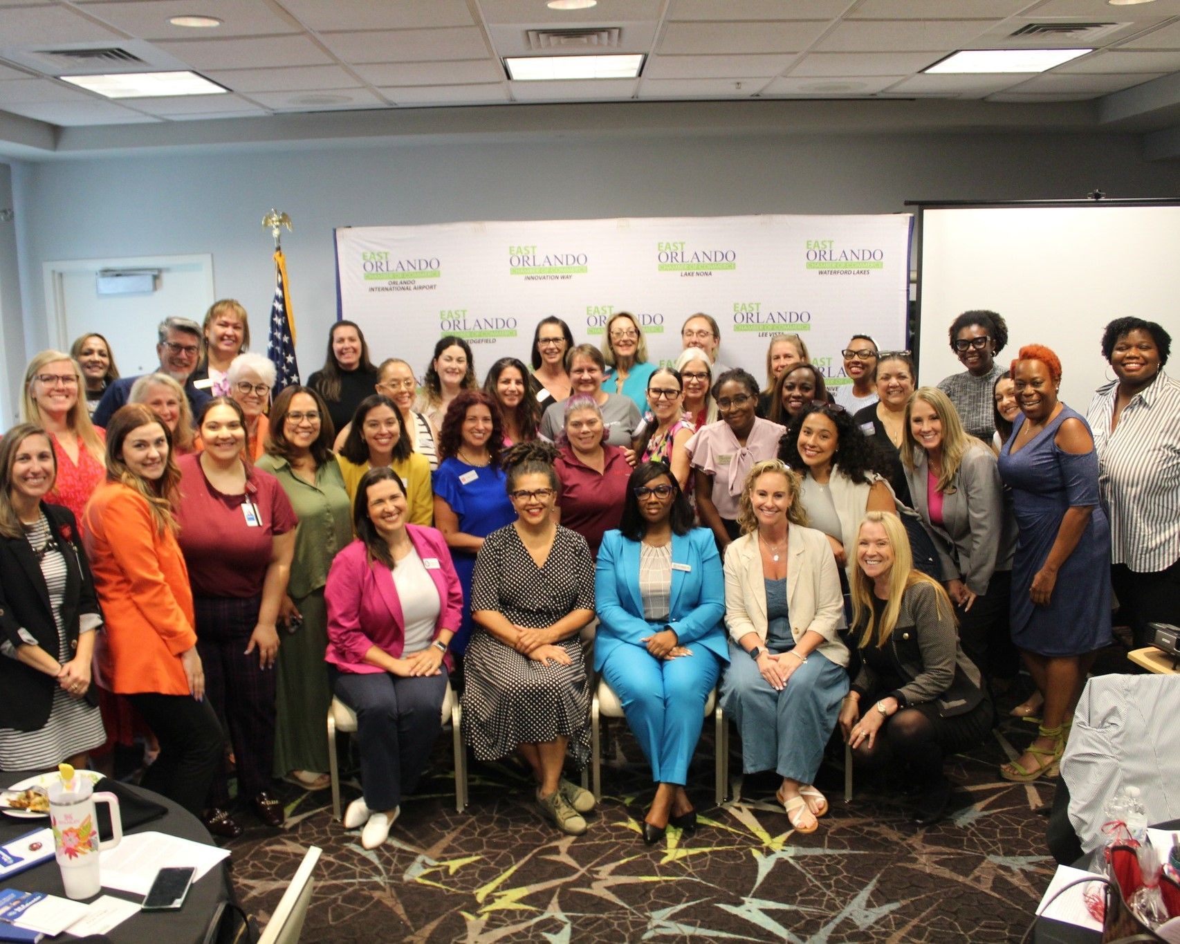 Group of people posing for a photo in a conference room with a banner; neutral expressions.