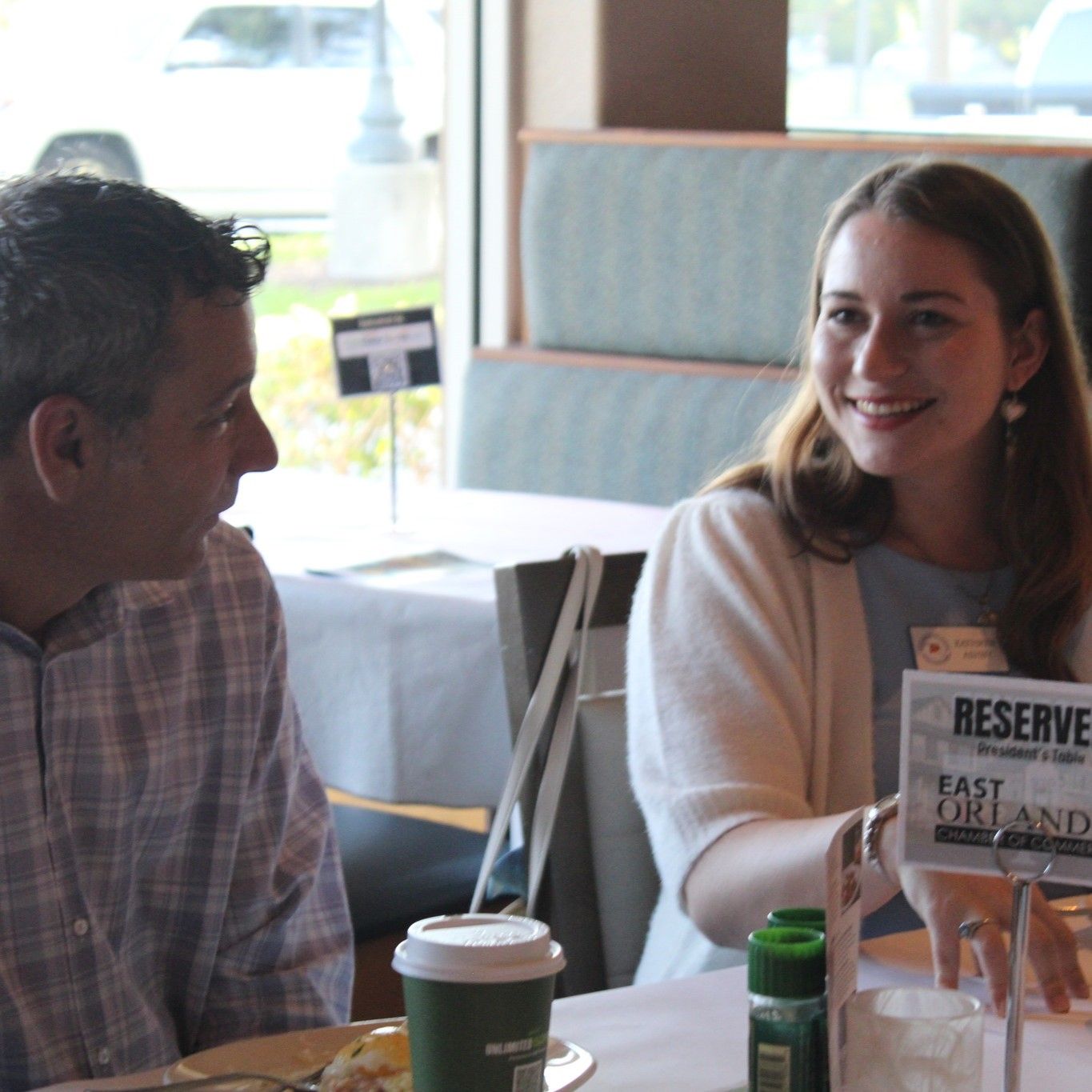 Woman smiles while talking to a man at a table in a restaurant; reserved sign visible.