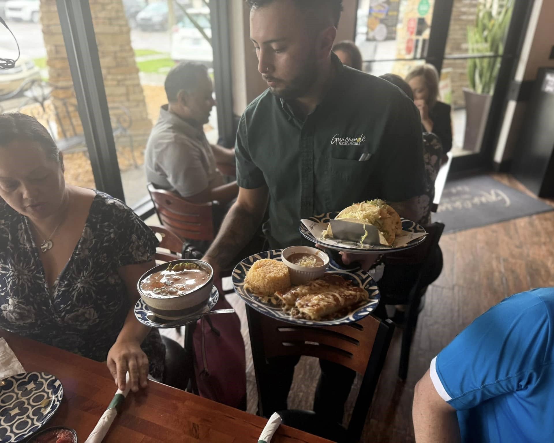 Waiter carrying plates of food in a restaurant, serving customers seated at tables.