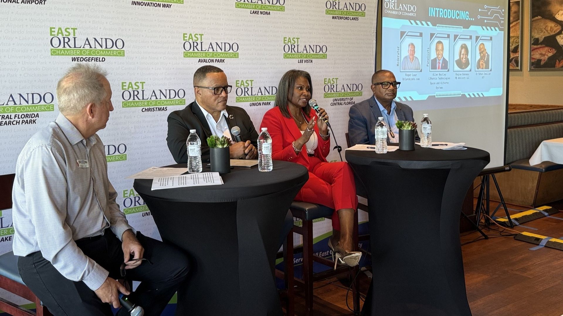 Panel discussion with four people seated at a table, East Orlando banner in background.