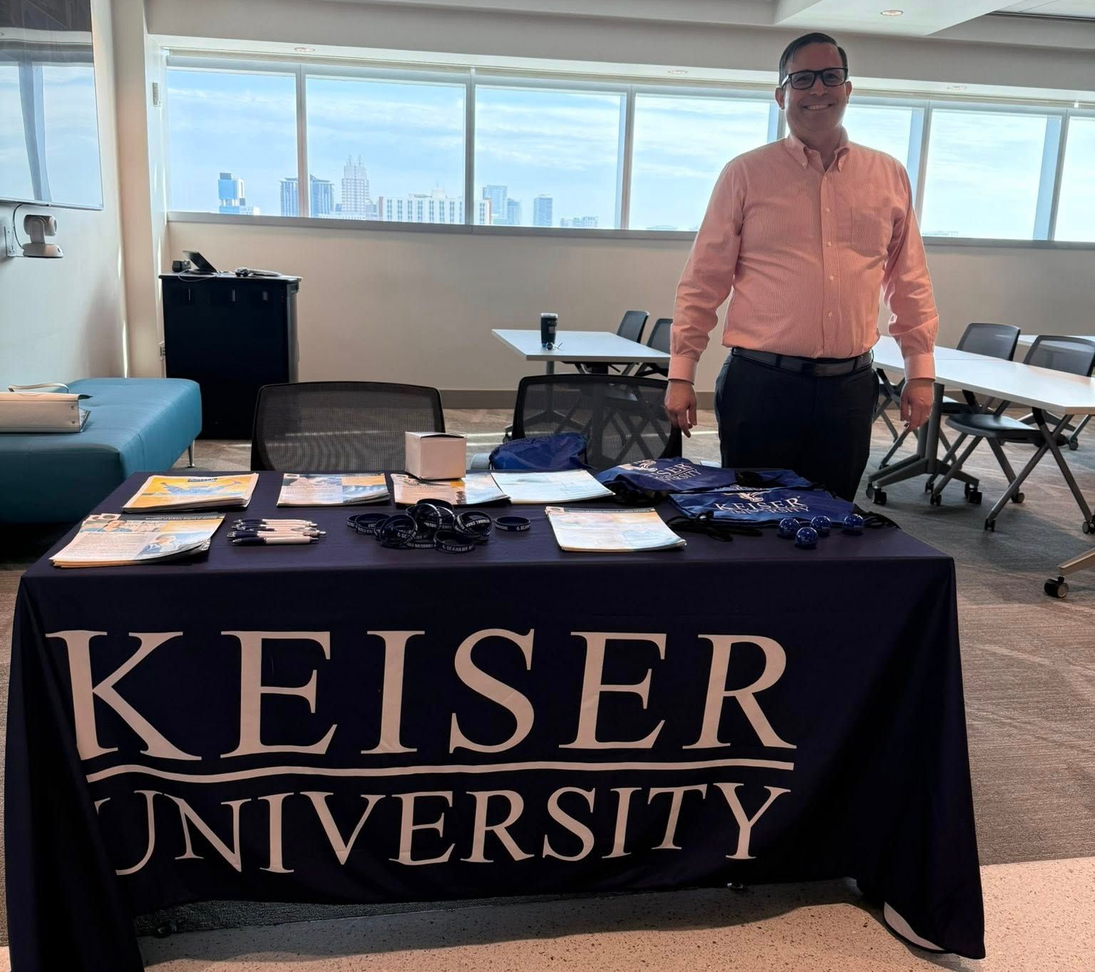Man at Keiser University information table, with city view background.