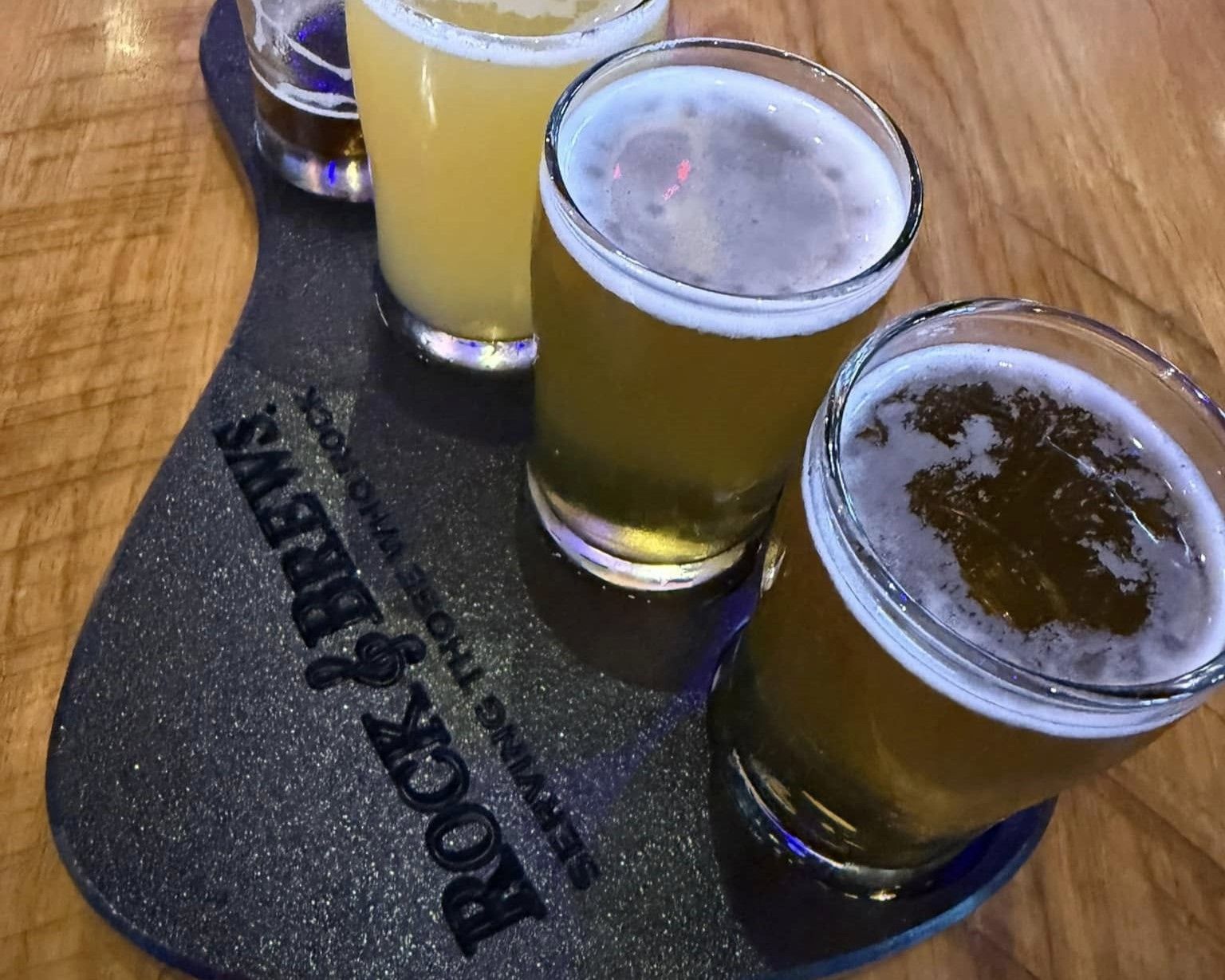 A flight of beers on a guitar-shaped serving board. Various shades of gold and amber.