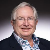 Smiling man with glasses wearing a floral shirt and navy blazer.