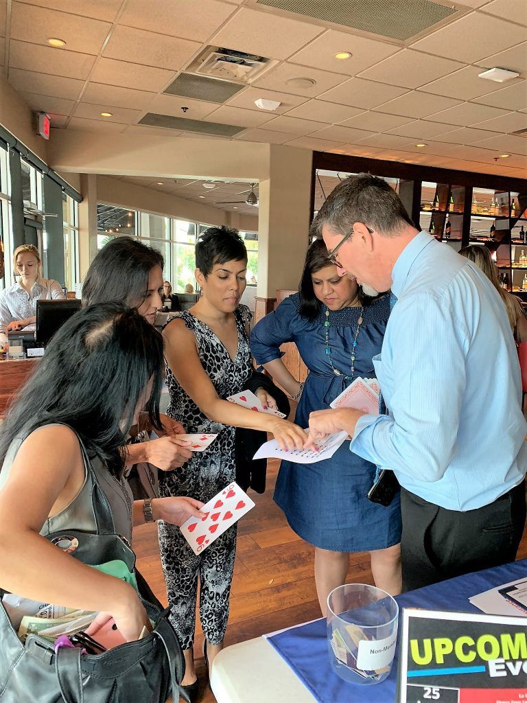Group of people looking at playing cards at a table with a man, in a restaurant setting.