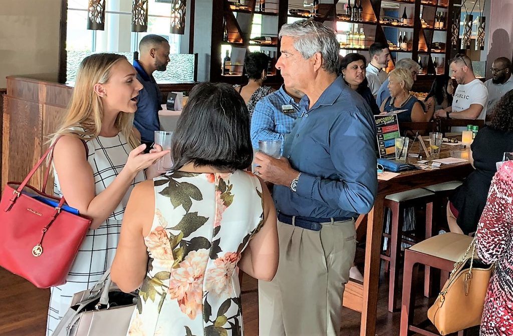 People talking and mingling at a bar, some holding drinks.