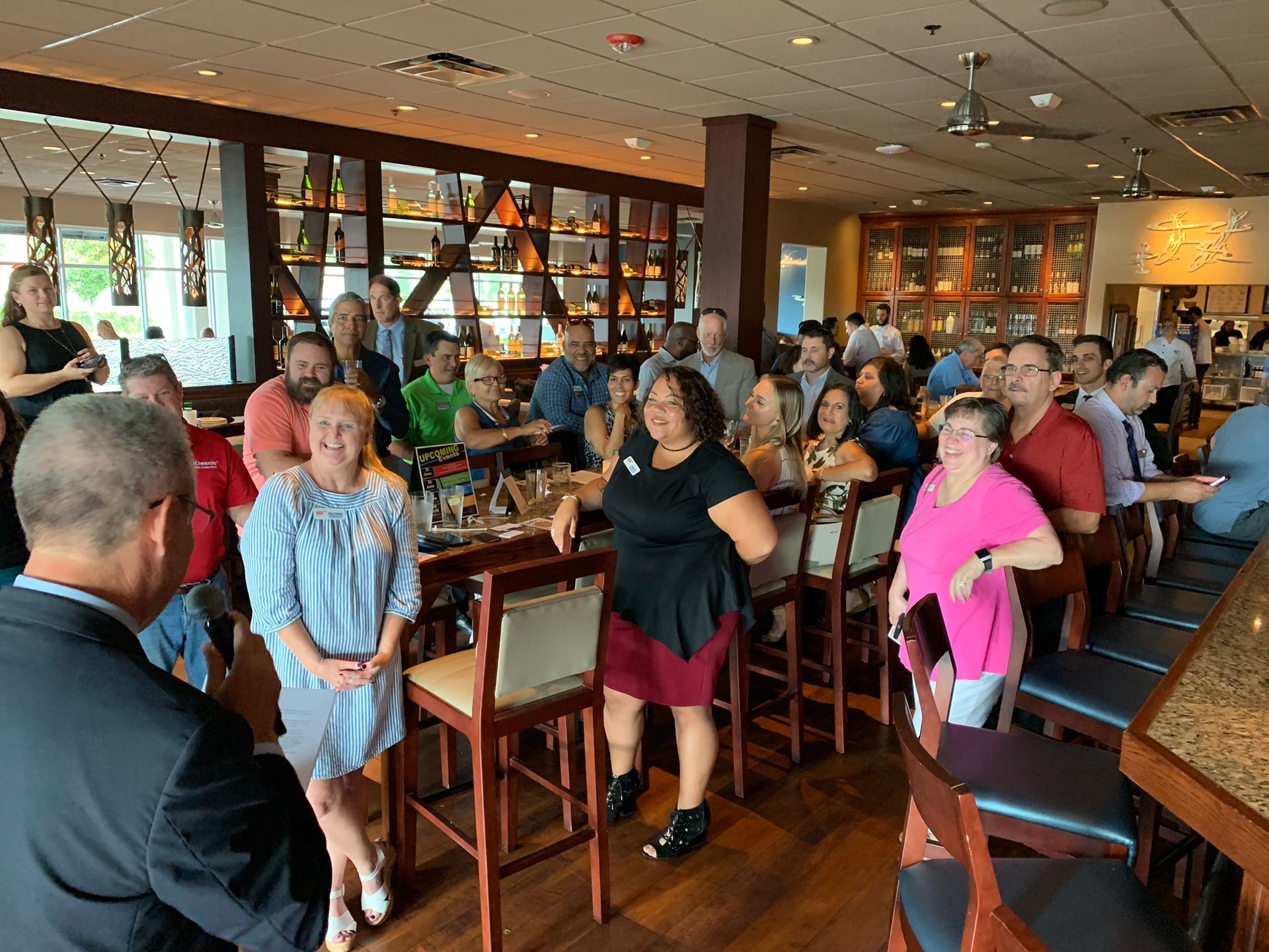 People gathered at a restaurant, some standing near a bar and tables. Several people are smiling.