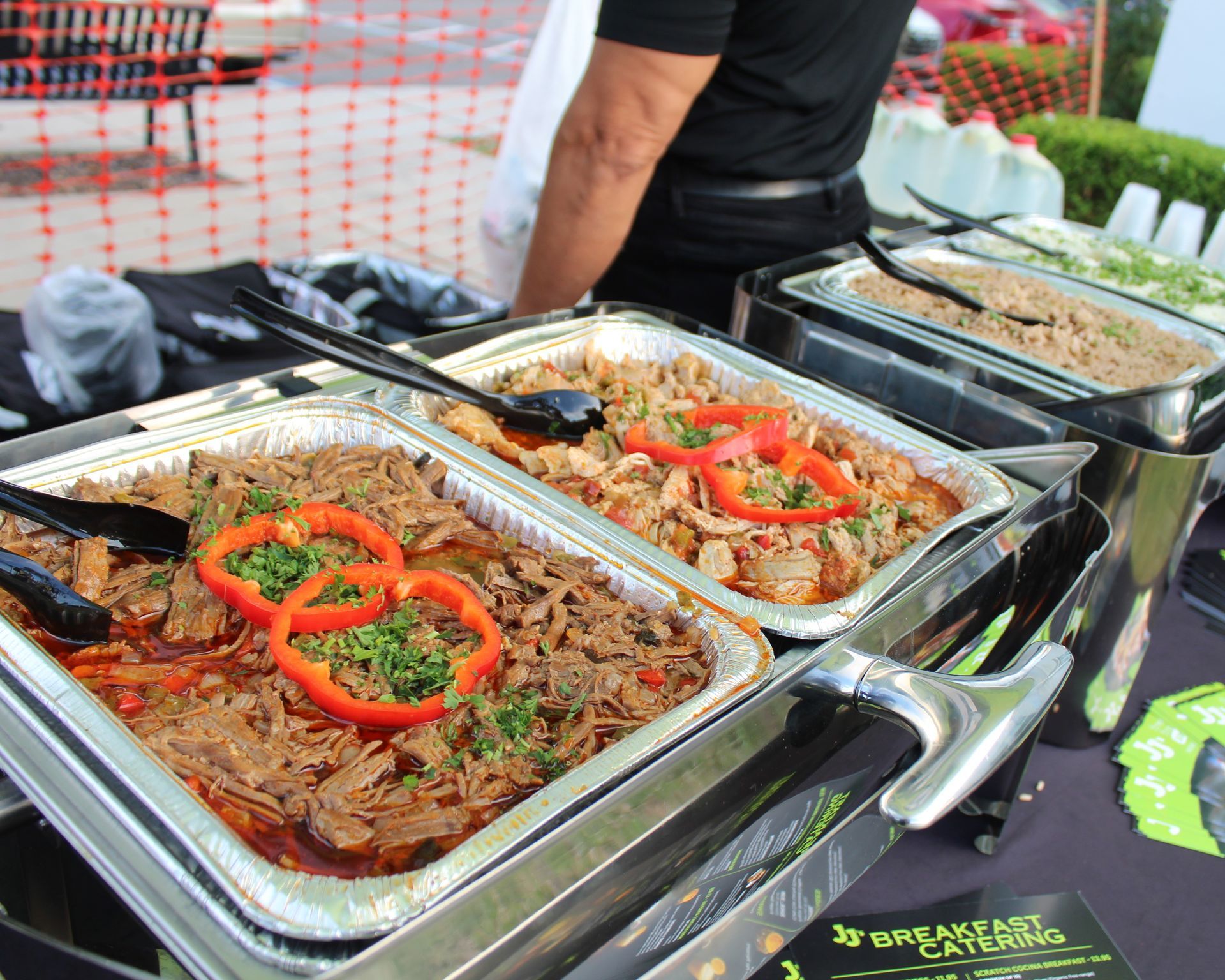 Buffet with various dishes including shredded meat topped with red peppers, in metal trays.