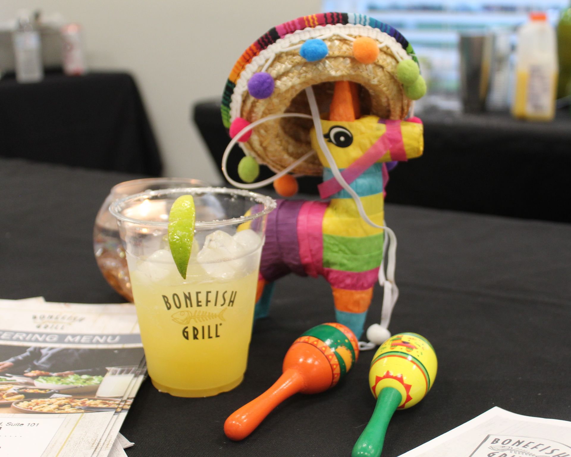 A margarita, pinata, and maracas on a table, with a catering menu in the background.