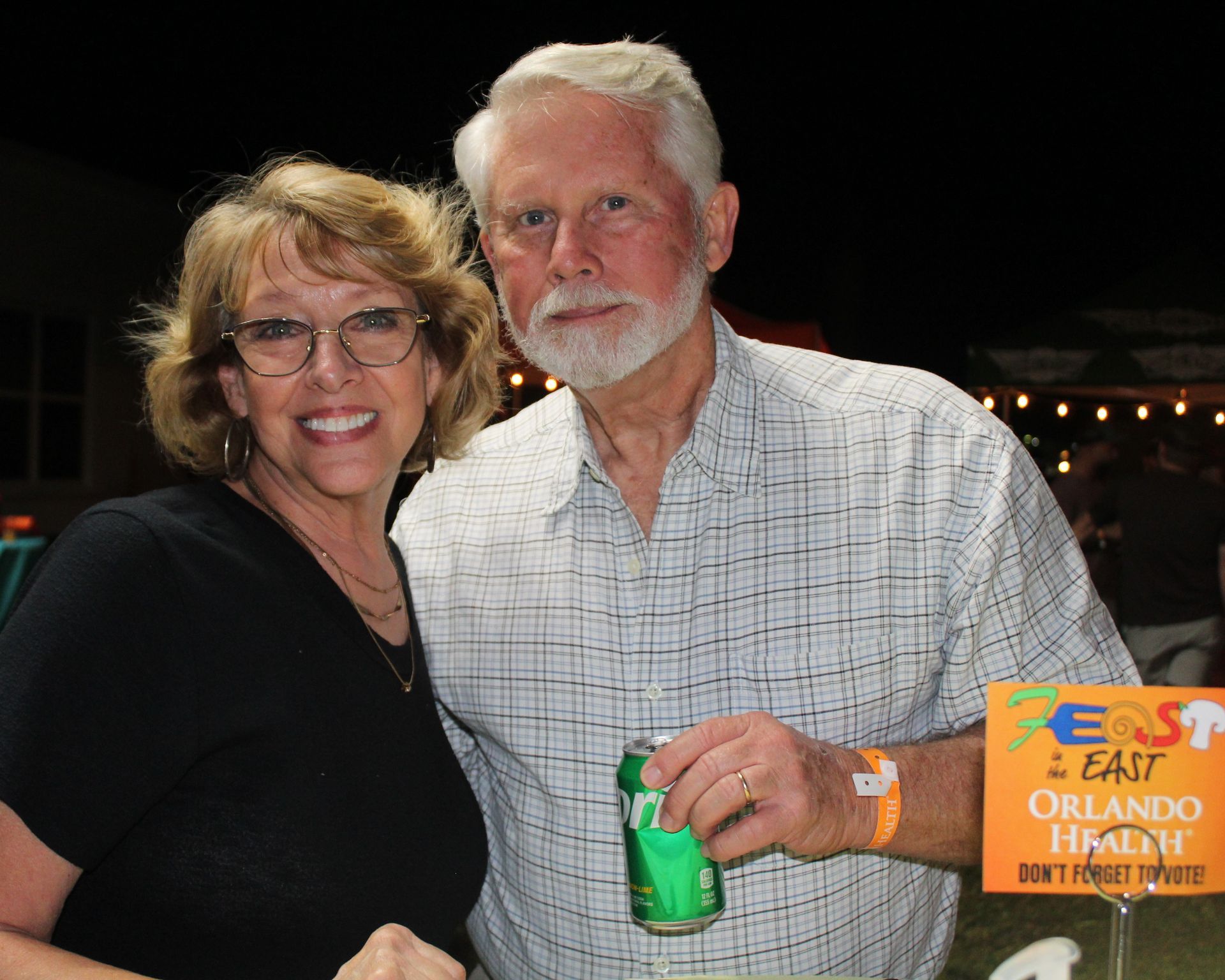 Woman and man smiling, posing for photo at outdoor event, man holding beverage.