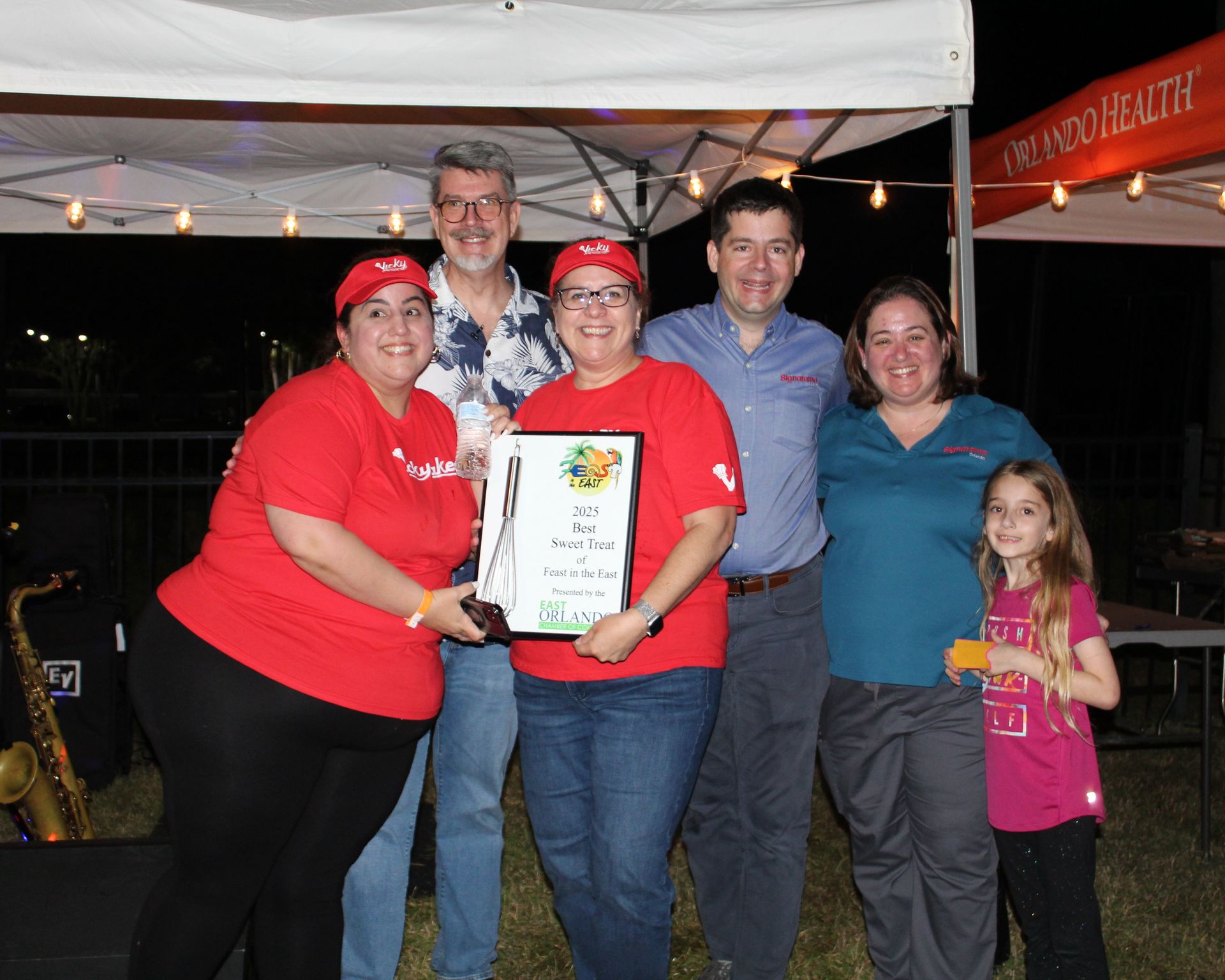Group holds an award. People smile in front of a tent. Night setting.
