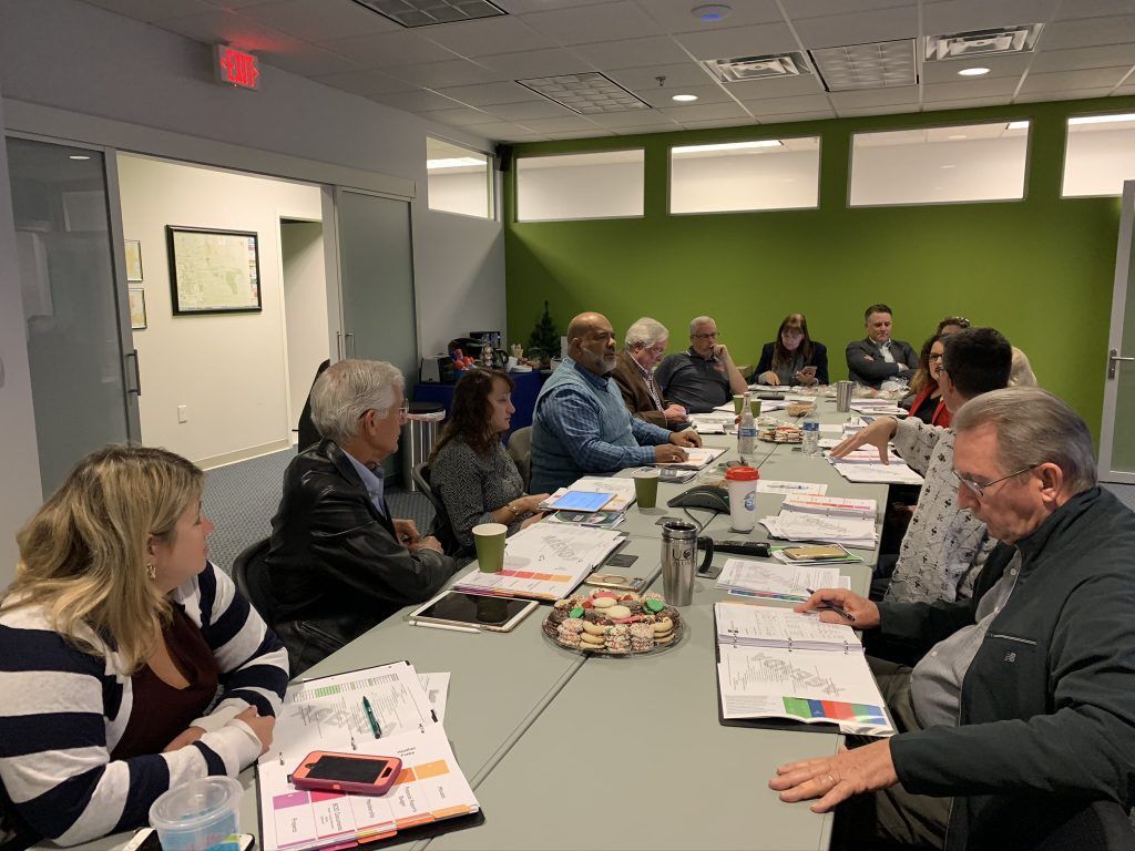 People seated at a table in a meeting room, looking at papers. Green wall in the background.