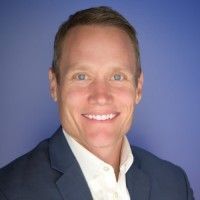 Man in a blue blazer and white shirt smiles at the camera against a blue backdrop.
