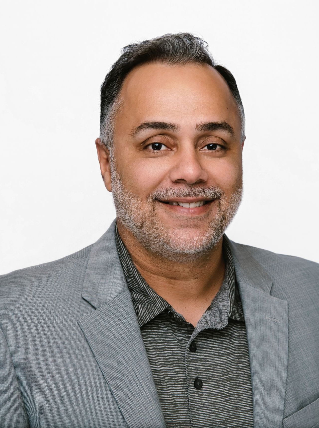 Man in gray blazer and textured shirt smiling at the camera.