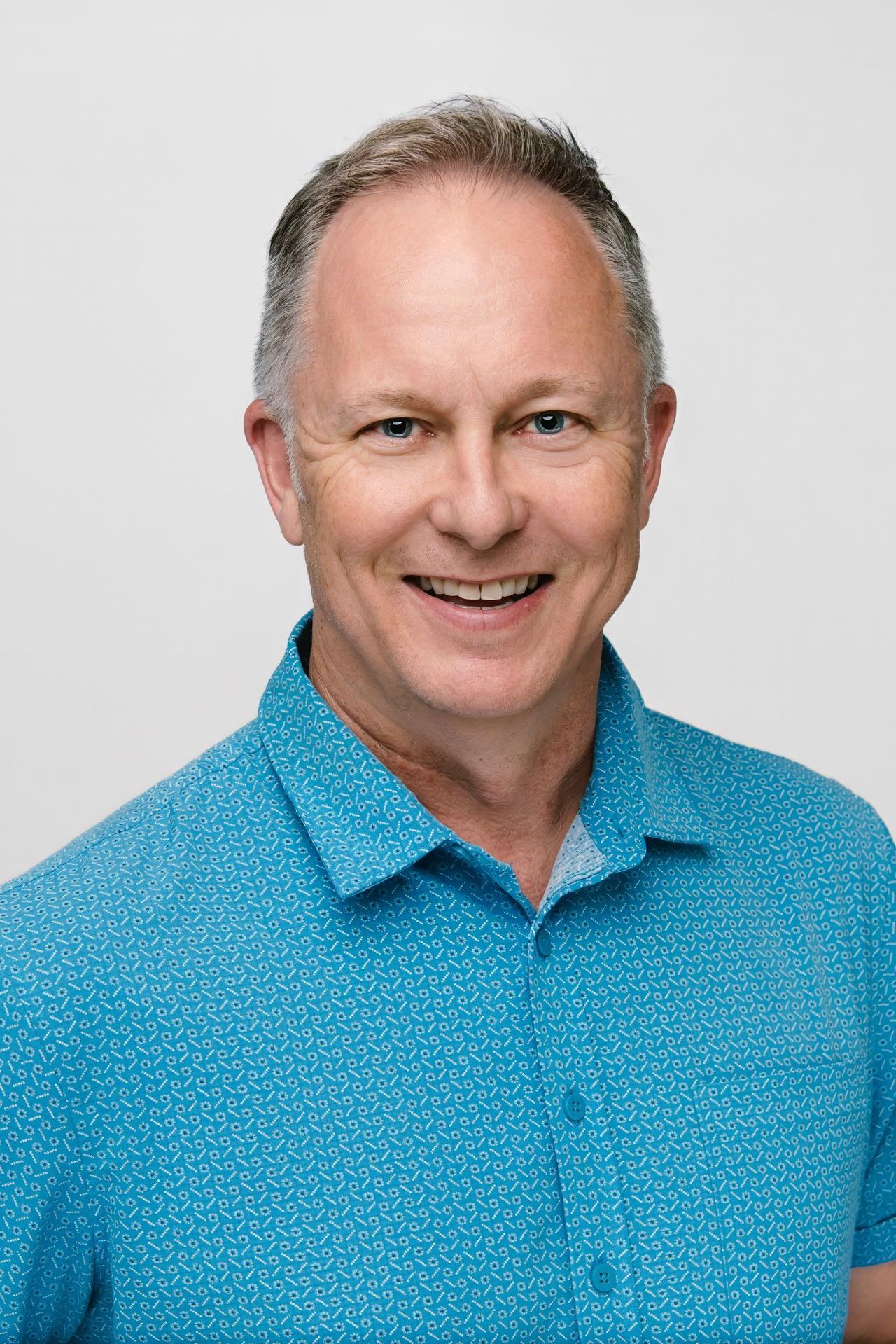 Man smiling, wearing a blue button-down shirt, against a white background.