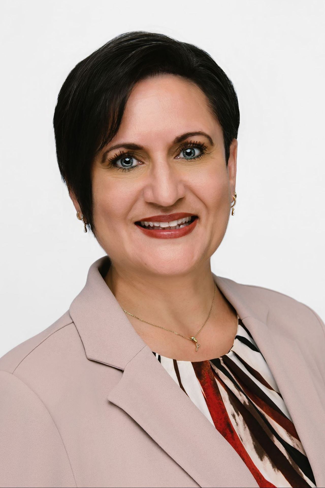Woman in a light blazer smiles, wearing a patterned top, set against a white background.